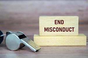 End Misconduct text on wooden blocks with whistle background. Whistleblow concept. photo