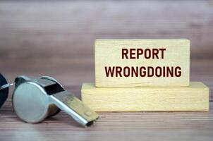 Report Wrongdoing text on wooden blocks with whistle. Whistleblow concept photo
