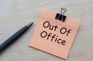 Top view of out of office text on notepad on wooden table photo