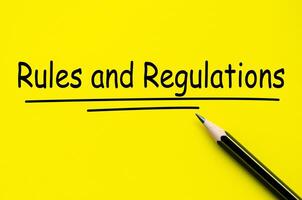 Rules and Regulation text on yellow notepad with pencil background photo