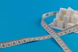 Sugar cubes on a white plate with measuring tape on a blue background photo