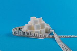Sugar cubes arranged in a pyramid beside a measuring tape on a blue background photo