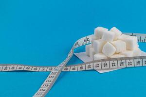 Sugar cubes with measuring tape on a blue background for kitchen use photo