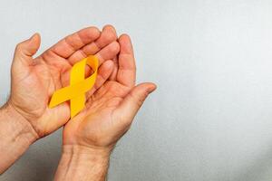 Support for cancer awareness with a symbolic yellow ribbon in hands photo
