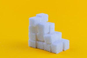 Stacked sugar cubes form a pyramid on a bright yellow background photo