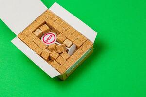 Stop sign surrounded by sugar cubes in a white box on bright green background photo