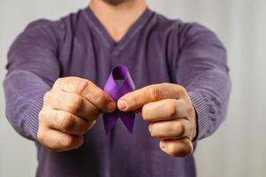 Person holds a purple ribbon symbolizing awareness in a simple setting photo