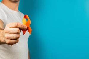 Person holds orange ribbon for mental health on blue background photo