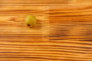 Green olive resting on a wooden surface with natural grain pattern photo