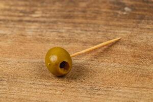 Enjoying a green olive on a toothpick resting on a wooden table photo