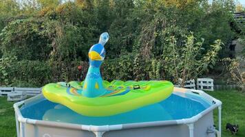 An inflatable mattress in the shape of a peacock floats on the water in a frame pool. video