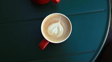Handheld static shot of cute latte art in black cup on green table video
