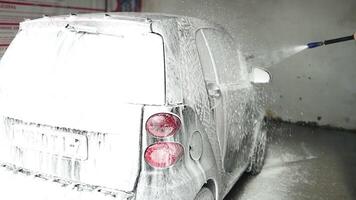 Man applying foam to black car in car wash. Car wash service with self-service option, foam sliding down the glass video