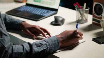 African American person working remotely and drafting project notes, organizing files and browsing web for relevant information. Comfortable home office setup for telework productivity. Camera B. video