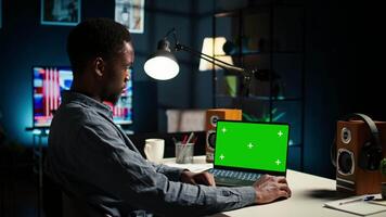 Black man creating a report with data next to isolated chroma key display, improving his skills and achieving career independence. Remote worker solving daily freelance tasks. Camera A. video