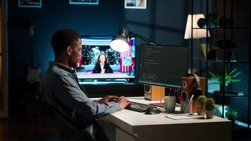 African american expert at desk using pc for programming and data analysis. Young networking expert working from his home setup, manages information technology and data center. Camera B. video