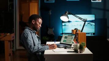African American teleworker managing daily schedule and does post it memo notes, creating a reminder to ensure task completion from his home office. Freelancer improving productivity. Camera B. video