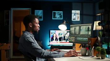 Young man editor works on editing film footage at home setup, doing freelance contract for post production scenes. Editor correcting white balance and color grading, pc software. Camera A. video