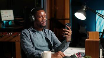 African american man waving and attending a web meeting from his urban apartment. Engaged male freelancer discussing work remotely with coworkers using wireless for conferencing call. Camera B. video