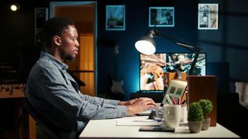 African American freelancer researching data driven topics at his home workstation, planning work schedule and completing project tasks. Managing job from a comfortable setup. Camera A. video