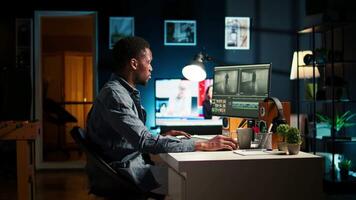 Focused male editor working on montage in a creative software at home office setup, digital media content. Filmmaker using dual monitors to edit footage in post production. Camera A. video