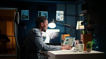 Black young adult working remotely and organizing information, reviewing notes and making data driven decisions to complete his freelancing tasks. Managing his schedule efficiently. Camera A. video