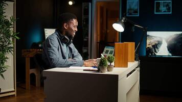 African american freelancer solving daily tasks with music on headset, listening to groovy songs and dancing at home office. Young adult enjoys multitasking with audio, self employed. Camera A. video