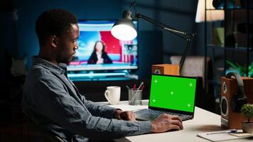 Black man creating a report with data next to isolated chroma key display, improving his skills and achieving career independence. Remote worker solving daily freelance tasks. Camera B. video