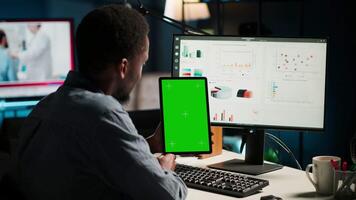Young guy examining funds for a program and holding tablet with mockup, studying finances and accounting management on a software. Male specialist doing remote work for a startup. Camera B. video