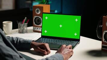 African american man working from home with green screen on laptop, looking at data on the web. Remote worker in personal apartment office crosschecking important info. Camera B. video
