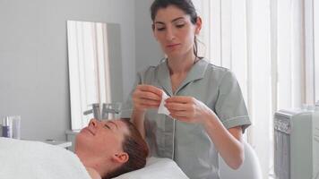 Cosmetologist applying sheet mask on woman face at spa studio video