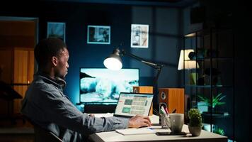 Financial manager doing remote accounting work with music on headset, solving his tasks on laptop at home. African american guy multitasking with his favorite playlist to help him focus. Camera A. video