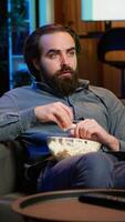 Vertical Man at home shocked by thriller film ending on TV, dropping popcorn out of mouth. Stupefied person at home left with eyes wide open by dramatic plot twist, watching suspenseful movie on TVV, camera A video