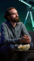 Vertical Man at home on couch gripped by interesting film shown on television screen. Person streaming content in neon lit living room, fascinated by entertaining movie scene, paying attention, camera A video