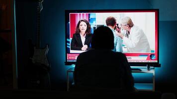 Curious spectator reading news coverage titles on smart tv set, sitting on couch and listening to journalist lay out recent global events. Guy watching daily news headlines, tv content. Camera B. video