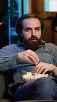Vertical Man at home looking in disbelief at thriller film on TV, stuffing mouth with popcorn. Stupefied person at home watching suspenseful movie on VOD channel, perplexed by plot twist, camera A video