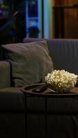 Vertical Bowl of popcorn on table next to remote control in neon illuminated apartment home theater. Close up shot of snack prepared for upcoming movie night in living room during leisure time video