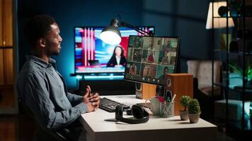 Black guy meeting with group of individuals on web conference, uses technology for virtual communication. Freelancer working remotely, online meetings or classes in a cozy home. Camera B. video