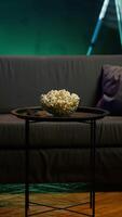 Vertical Cozy residential interior with sofa and snack setup, ready for casual movie night or immersive TV viewing experience. Bowl of popcorn on table in neon illuminated home theater apartment video