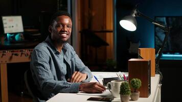 POV of african american guy attending an online conference from his home office in loft. Male speaker discussing work remotely with coworkers using wireless tech for call. Camera B. video