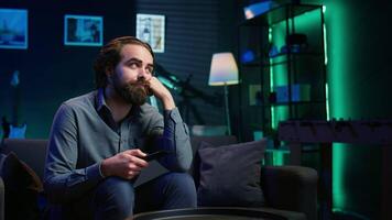 Man bored at home searching for TV series to binge on streaming services, procrastinating. Close up of person sitting on couch, flipping though TV channels using remote control, camera B video
