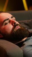 Vertical Gamer lounged on couch focused on winning competitive multiplayer game eating popcorn. Person in home theatre holding controller munching on salty snack, playing videogames, camera A video