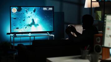 Guy spends time on television playing multiplayer web games, setting his console into smart tv and having fun gaming at night. Player battling in shooter competition. Camera B. video