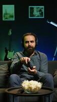 Vertical Gamer wearing headphones frustrated after getting game over message while playing videogame, raging. Man gaming with controller at home angry after losing level, camera B video