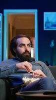 Vertical Man at home shocked by thriller film ending on TV, dropping popcorn out of mouth. Stupefied person at home left with eyes wide open by dramatic plot twist, watching suspenseful movie on TV, camera B video