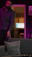 Vertical Happy person arriving home, excited to do gaming during leisure time. Cheerful player entering room, jumping on couch, excited to play videogame on console, relaxing after hard day at work video