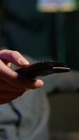 Vertical Close up of device used by person to scroll through streaming content, picking movie. Focus on remote control used by man in blurry background switching channels on television screen, camera A video
