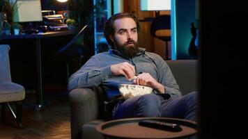 Man at home shocked by thriller film ending on TV, dropping popcorn out of mouth. Stupefied person at home left with eyes wide open by dramatic plot twist, watching suspenseful movie on TVV, camera A video