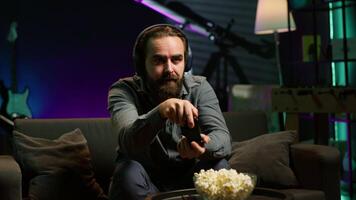 Man looking in disbelief at TV screen while playing videogames, receiving game over message on gaming console. Gamer upset after being defeated by rival players in online esports competition, camera A video