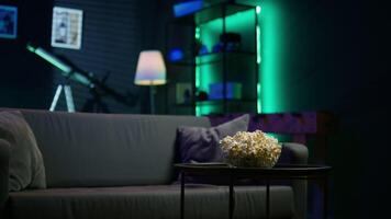 Apartment room with dimmed lighting, popcorn and remote on small table, creating relaxed mood for movie night, close up. Panning shot of popcorn bowl on table in living room video